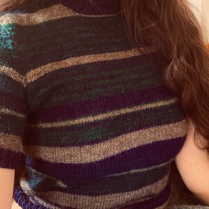 May include: A striped sweater with brown, green, and purple stripes. The sweater is knit and has a crew neck.