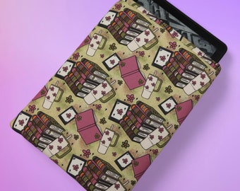 Puede incluir: Una funda para lector electrónico de patrón verde y marrón con una pila de libros, tazas de café y flores. La funda está diseñada para adaptarse a un Kindle u otro lector electrónico.