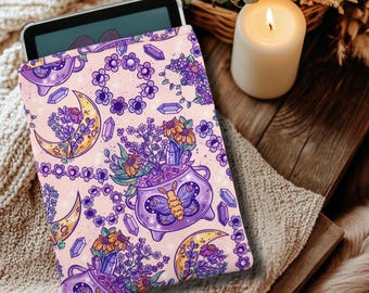 Könnte beinhalten: Eine violette und rosafarbene Tablethülle mit einem verspielten Design, das einen Kessel zeigt, der mit Blumen, Kristallen und einem Schmetterling gefüllt ist. Der Hintergrund ist hellrosa mit einem sich wiederholenden Muster aus Monden, Blumen und Kristallen.