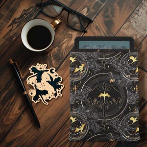 May include: A black e-reader cover with a gold and white design featuring dragons and clouds. The design is repeated on the cover.