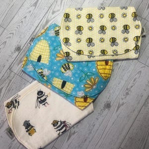 May include: Three cloth diaper changing pads with bee and honeycomb patterns. One pad is light yellow with bee and flower designs. Another is blue with bees, honeycombs, and flowers. The third is off-white with cartoon bees.
