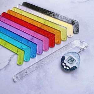 Puede incluir: Un conjunto de 10 marcapáginas de purpurina de colores con un marcapáginas de purpurina transparente y un llavero Tamagotchi azul y blanco.