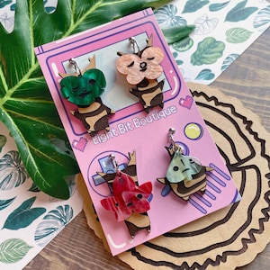 May include: Four dangle earrings featuring wooden bodies with striped patterns and colorful acrylic leaf-shaped tops. The earrings are displayed on a pink card labeled Eight Bit Boutique with pixelated heart and game controller graphics.