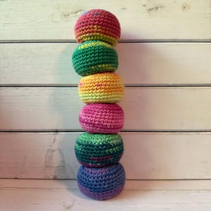 May include: A stack of six handmade crochet balls in a variety of colors, including red, green, yellow, pink, and blue. The balls are stacked vertically against a white wooden background. Each ball is approximately 3 inches in diameter.