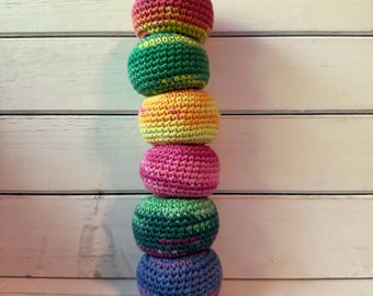 May include: A stack of six handmade crochet balls in a variety of colors, including red, green, yellow, pink, and blue. The balls are stacked vertically against a white wooden background. Each ball is approximately 3 inches in diameter.