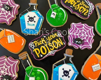 May include: A selection of Halloween biscuits, featuring potion bottles with skull and crossbones, spiderwebs with spiders, and text that reads "Poison" and "Pick your Poison". The biscuits are decorated with bright colours.