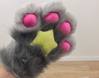Puede incluir: Una pata de felpa gris con almohadillas de color rosa brillante y un acento en forma de estrella amarilla. La pata de piel sintética tiene un puño y está diseñada para usarse en la mano. La pata es un accesorio caprichoso.