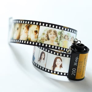 Op de afbeelding: Een zwarte en gele filmdoos sleutelhanger met een 35mm kleurenfilm label. De doos heeft een zwart-witte filmstrip eraan bevestigd met foto's van kinderen.
