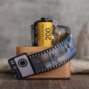 May include: A wooden box with a film strip keychain attached to the top. The keychain is made of a black and white film strip with photos of people. The box has a label that says "Memory" and a small camera icon. The film strip keychain has a yellow film canister attached to it with the text "200 36 exp. Kodak 200.36 PROCESS C-41 35mm colr print film 200".