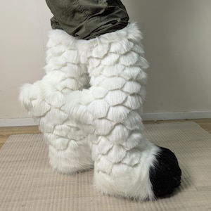 May include: White faux fur costume legs with a scale-like pattern. The feet are black and white. The legs are worn with olive green trousers.