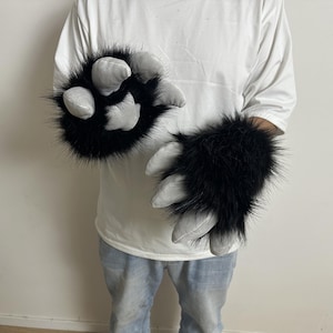 Puede incluir: Un par de guantes de pata de monstruo peludos negros y grises. Los guantes tienen pelo largo negro y garras acolchadas grises. Los guantes están diseñados para usarse en las manos y son un accesorio de disfraz.