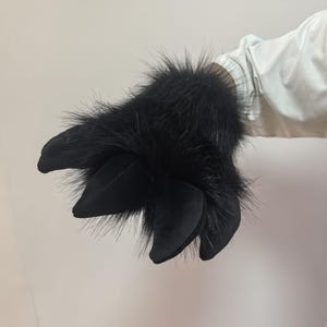 May include: A black furry monster claw with four large, rounded, black claws. The claw has long, black fur around the base of the claws. The item is likely a costume accessory.