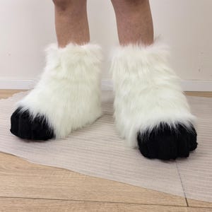 May include: White furry boots with black paw-like bottoms. The boots are made of soft, fluffy material and cover the feet and ankles. These novelty boots are a fun costume accessory.