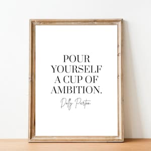 May include: A framed print with a black and white quote that reads "Pour yourself a cup of ambition." The quote is attributed to Dolly Parton.