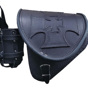May include: Black leather motorcycle saddlebag with a water bottle holder. The saddlebag features a large, embossed Maltese cross design. The bag has a curved shape and is secured with a buckle. The water bottle holder is attached.
