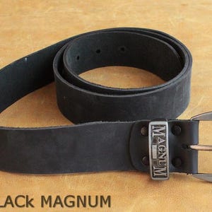 May include: A black leather belt with a silver buckle. The buckle is rectangular and features the word "MAGNUM". The belt is coiled on a light brown surface. The text "PA13 BLACK MAGNUM" is at the bottom.