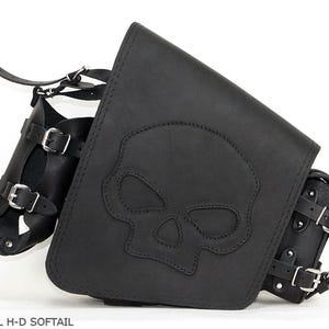 Op de afbeelding: Zwarte leren motorzadeltas met een schedelontwerp. De tas heeft meerdere compartimenten, verstelbare riemen en zilveren gespen. De tekst "S494 SKULL H-D SOFTAIL" is zichtbaar onderaan de afbeelding.