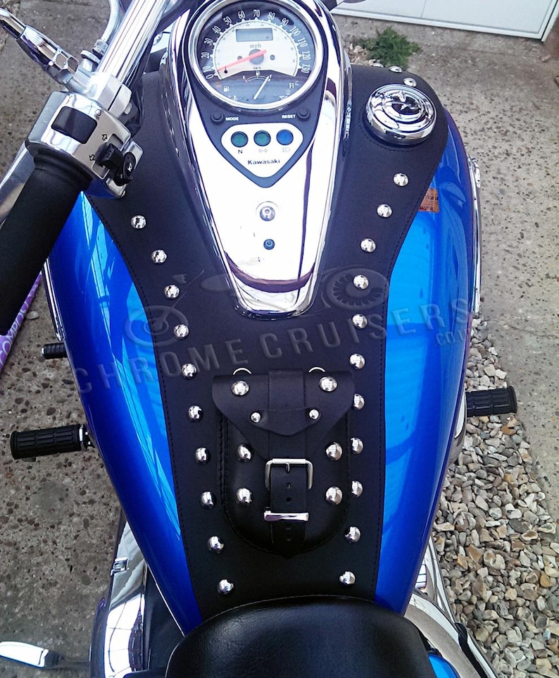 Puede incluir: Un tanque de gasolina de motocicleta azul con una cubierta de tanque de cuero negro tachonada con una peque&ntilde;a bolsa y una hebilla. La cubierta del tanque tiene el texto "CHROME CRUISERS" impreso en ella.