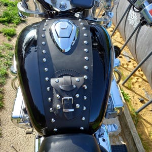 May include: Black motorcycle with a black leather gas tank cover with silver studs and a buckle. The cover has a decorative flap with a buckle.