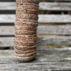 May include: A stack of small, speckled ceramic bowls in shades of brown and white. The bowls are stacked on a wooden surface.