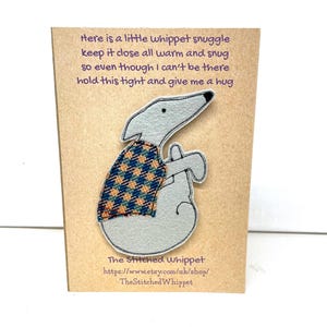 May include: A gray felt whippet dog pin wearing a plaid vest, attached to a brown card. Text on the card reads, "Here is a little whippet snuggle...hold this tight and give me a hug." The shop name and URL are also printed.