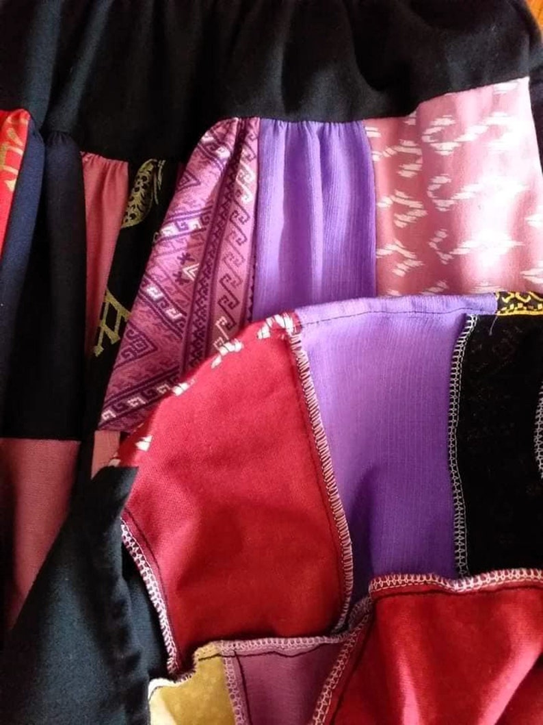 K&ouml;nnte beinhalten: Ein Patchwork-Rock aus verschiedenen Stoffen in Rot-, Lila-, Rosa- und Schwarzt&ouml;nen. Der Rock hat eine Vielzahl von Mustern, darunter geometrische Designs und Blumenmuster.