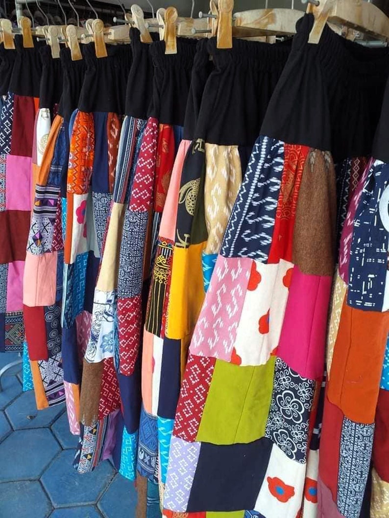 K&ouml;nnte beinhalten: Eine Sammlung bunter Patchworkr&ouml;cke mit einem schwarzen Bund. Die R&ouml;cke bestehen aus verschiedenen Stoffen, darunter Blumenmuster, geometrische Muster und einfarbige Stoffe.