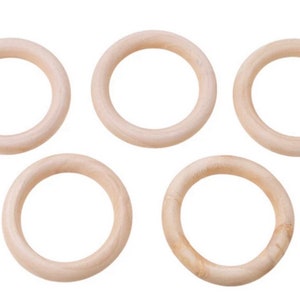 Könnte beinhalten: Fünf unfertige Holzringe, jeweils mit kreisförmiger Form und hellbeiger Farbe. Die Ringe bestehen aus Naturholz und sind vor einem weißen Hintergrund angeordnet. Diese Ringe eignen sich für verschiedene Bastelprojekte.