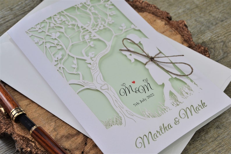 Laser cut wedding invitation in white and mint colour.
Married couple under the tree laser cut at the front of the invitation. Names of the couple laser cut at the bottom.