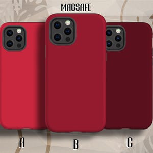 Op de afbeelding: Drie effen gekleurde telefoonhoesjes in roodtinten. De hoesjes zijn gelabeld met A, B en C, met het woord "MAGSAFE" bovenaan. Elk hoesje heeft een camera-uitsparing en een gladde, matte afwerking.