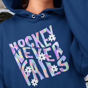 Könnte beinhalten: Ein blauer Hoodie mit einer bunten Grafik, auf der "Hockey Never Fails" steht, mit weißen Blumen um den Text herum.