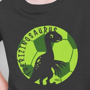 May include: Black t-shirt with a green soccer ball graphic featuring a black silhouette of a Therizinosaurus dinosaur. The text "The Therizinosaurus" is written around the ball.