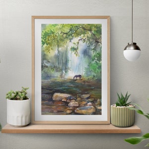 Könnte beinhalten: Aquarellmalerei einer Wasserfallszene mit einem Pferd, das aus dem Wasser trinkt. Das Kunstwerk ist in einem hellen Holzrahmen gerahmt und auf einem Holzregal mit Pflanzen ausgestellt. Das Gemälde zeigt üppiges grünes Laub und eine ruhige Atmosphäre.