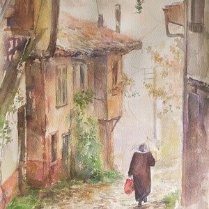 May include: Watercolor painting of a European street scene on a rainy day. A person with an umbrella walks down a cobblestone street, carrying a red bag. Buildings with red tile roofs and vines are on either side.