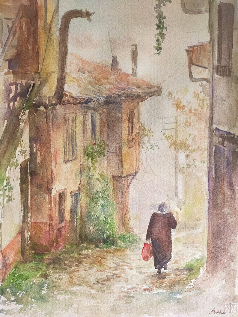 May include: Watercolor painting of a European street scene on a rainy day. A person with an umbrella walks down a cobblestone street, carrying a red bag. Buildings with red tile roofs and vines are on either side.