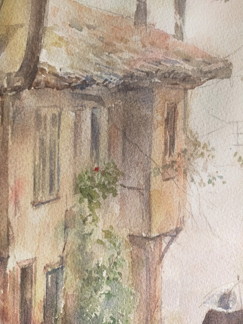 May include: Watercolor painting of a weathered building with a tiled roof and small windows. The building's facade is a warm beige, with hints of pink and brown. Green foliage and a red flower add a touch of color to the scene.