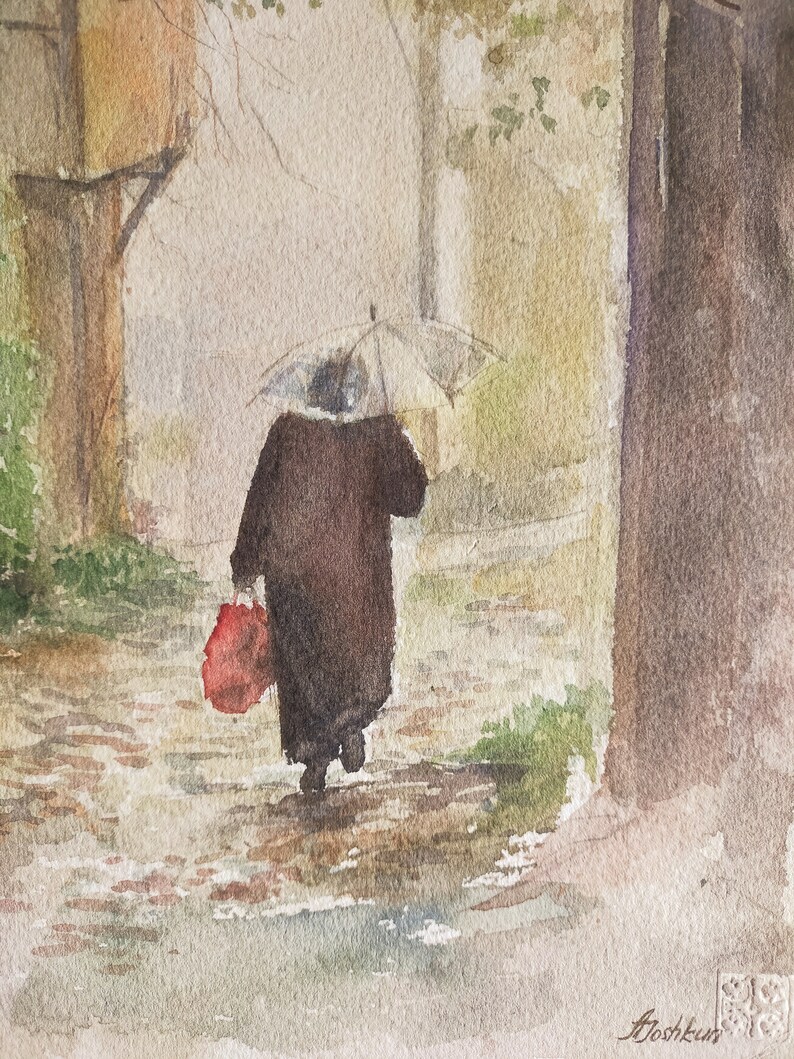 May include: Watercolor painting of a person walking in the rain under a clear umbrella. The person is wearing a dark coat and carrying a red bag. The scene is set on a cobblestone street with buildings and trees in the background.