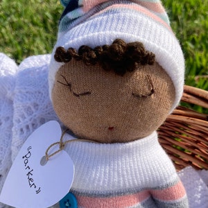 Peut inclure: Une poupée en chaussette faite à la main avec des cheveux bruns, portant un chapeau rayé blanc et bleu et une tenue rayée blanche et bleue. La poupée a une étiquette en forme de cœur qui dit "Parker".