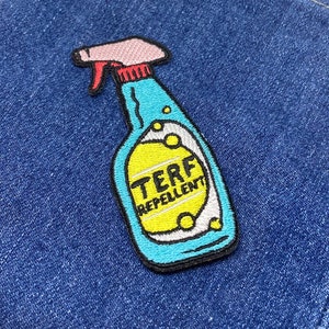 May include: Embroidered patch depicting a blue spray bottle with the text "TERF REPELLENT" on a yellow label. The patch has a pink nozzle and red trigger, set against a denim background.