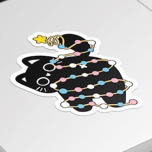 May include: A black cat with a white star on its head is tangled in a string of colorful Christmas lights. The lights are pink, blue, and white with a gold accent.