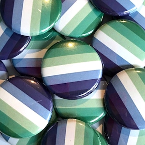 Puede incluir: Primer plano de un mont&oacute;n de botones redondos con un dise&ntilde;o a rayas verde, blanco, azul y morado. Los botones son todos del mismo tama&ntilde;o y est&aacute;n dispuestos en un patr&oacute;n aleatorio.