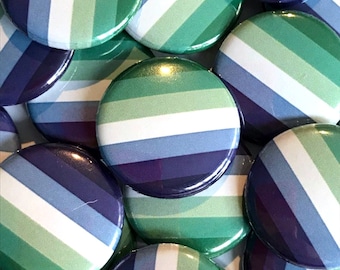 Può includere: Primo piano di un mucchio di bottoni rotondi con un designo a strisce verde, bianco, blu e viola. I bottoni sono tutti della stessa dimensione e sono disposti in uno schema casuale.