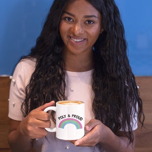 May include: White ceramic mug with a rainbow design and the text "POLY & PROUD" in black. The mug is filled with a light brown beverage.