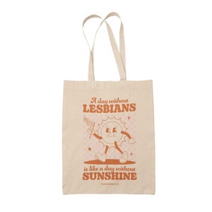 K&ouml;nnte beinhalten: Eine beige Tragetasche mit einer Comic-Sonne, die eine Regenbogenflagge h&auml;lt, und dem Text "A day without LESBIANS is like a day without SUNSHINE".