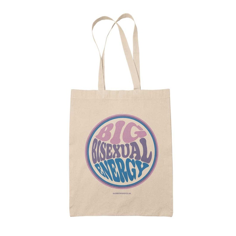 K&ouml;nnte beinhalten: Eine beige Tragetasche mit einem blauen, rosa und violetten Kreisdesign, auf dem "BIG BISEXUAL ENERGY" steht.