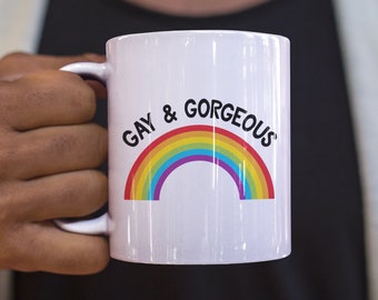 May include: White ceramic mug with a rainbow and the text "Gay & Gorgeous" printed on it.