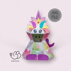 Può includere: Un calendario dell'avvento a forma di unicorno colorato con i numeri da 1 a 17 su ogni faccia. L'unicorno è fatto di carta e ha una criniera rosa, gialla, blu e verde. L'unicorno è seduto su uno sfondo bianco.