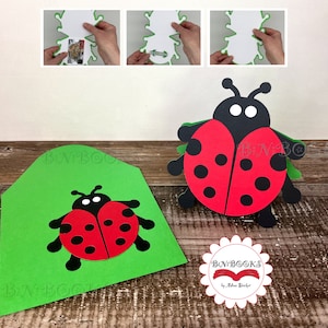 May include: A red and black ladybug pop-up card with green leaves. The card is folded and ready to be sent.