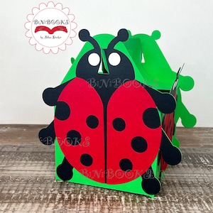May include: A green, red, and black ladybug-shaped box. The box has a red body with black spots and black antennae. The box is made of paper and has the text "BN BOOKS" on the side.