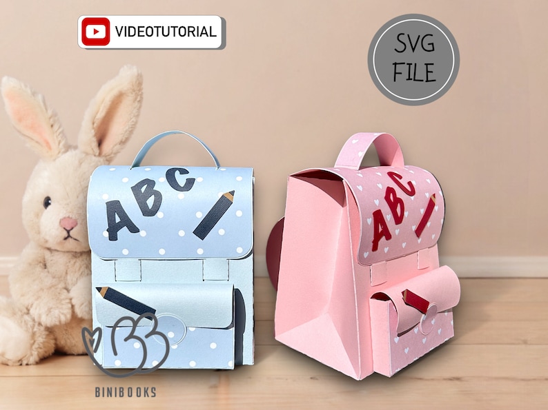 Puede incluir: Dos mochilas de papel, una azul con lunares blancos y la otra rosa con corazones blancos, ambas decoradas con las letras "ABC" y un l&aacute;piz. Las mochilas est&aacute;n dise&ntilde;adas para un proyecto de manualidades.